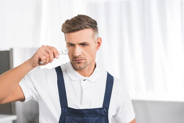 Thoughtful adult repairman holding and looking at wrench with screw — Stock Photo