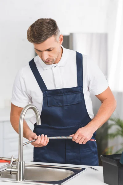 Adult repairman holding pipe while repairing faucet at kitchen — Stock Photo