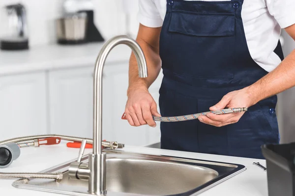 Vista ritagliata del riparatore che tiene il tubo nelle mani mentre ripara il rubinetto della cucina — Foto stock