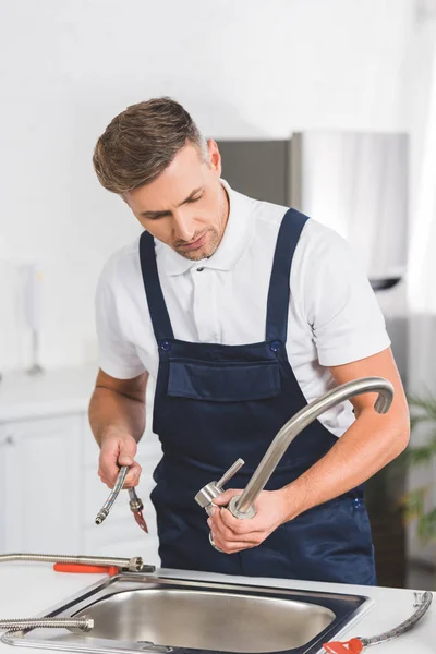 Adult repairman taking off kitchen faucet for repairing — Stock Photo