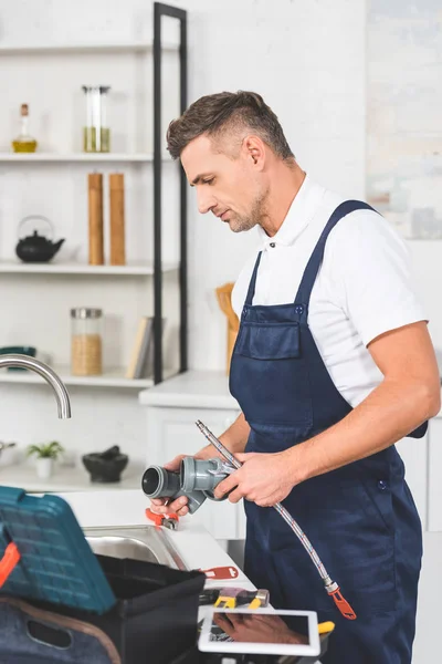 Perfil del reparador adulto que sostiene las tuberías para la reparación del grifo de la cocina - foto de stock