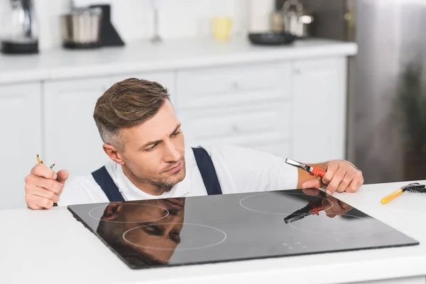 Thoughtful adult repairman repairing electric stove at kitchen — Stock Photo