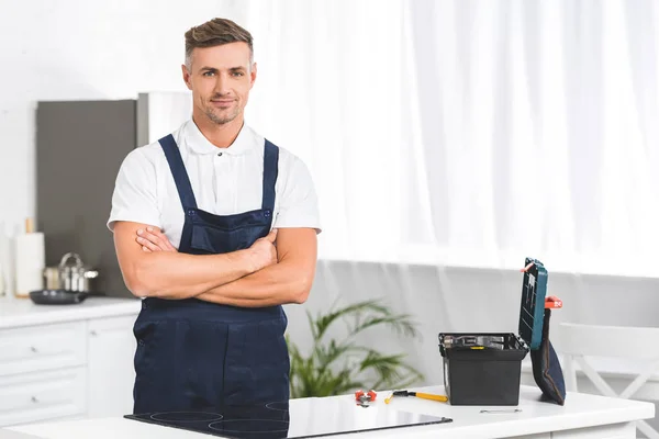 Erwachsener Reparateur steht neben Elektroherd mit gekreuzten Händen in Küche und blickt in Kamera — Stockfoto