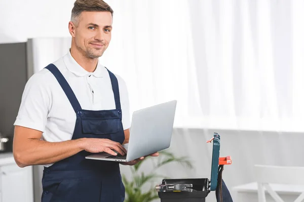 Erwachsener Reparateur hält Laptop in der Küche und schaut in die Kamera — Stockfoto