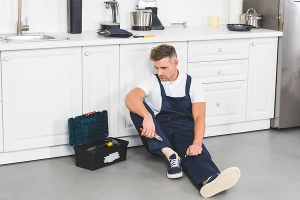 Reparador adulto trastornado sentado y sosteniendo alicates en la cocina - foto de stock