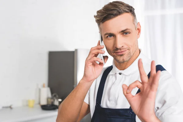 Adult repairman talking on smartphone and showing ok sign — Stock Photo