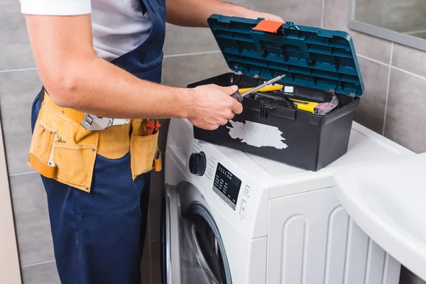 Vista recortada del reparador poniendo destornillador en la caja de herramientas en el baño - foto de stock