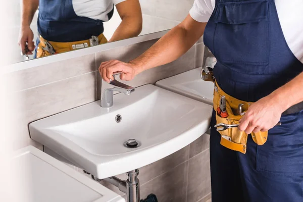 Ausgeschnittene Ansicht des Reparateurs, der nach der Reparatur den Wasserhahn überprüft und den Schlüssel hält — Stockfoto