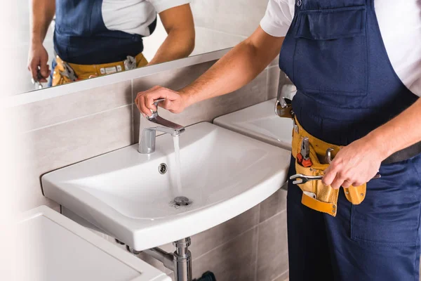 Ausgeschnittene Ansicht des Reparateurs, der nach der Reparatur den Wasserhahn überprüft und den Schlüssel hält — Stockfoto