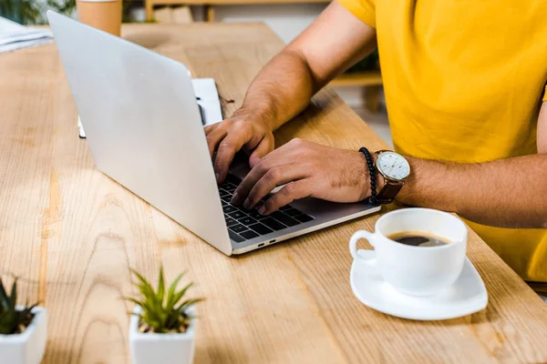 Cropped view of man typing on laptop near cup of coffee — Stock Photo