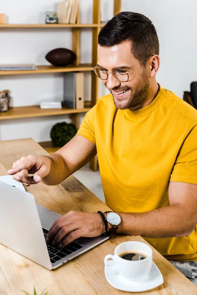 Hombre guapo señalando con el dedo a la computadora portátil en casa - foto de stock