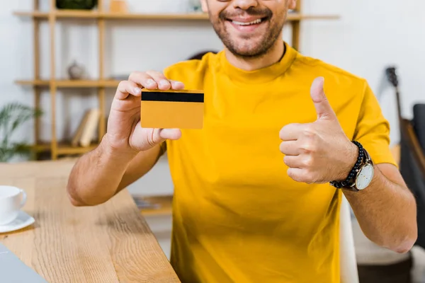 Vista recortada del hombre sosteniendo la tarjeta de crédito y mostrando el pulgar hacia arriba - foto de stock