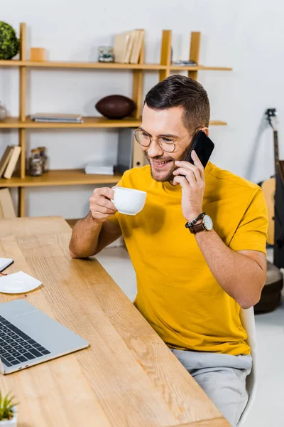 Bel homme en lunettes parlant sur smartphone et tenant une tasse de café — Photo de stock