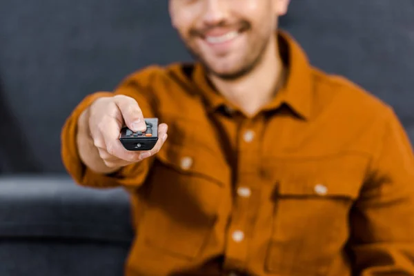 Selective focus of remote control in hand of cheerful man — Stock Photo