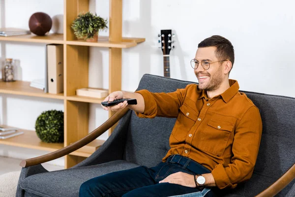 Handsome man sitting on sofa and holding remote control — Stock Photo