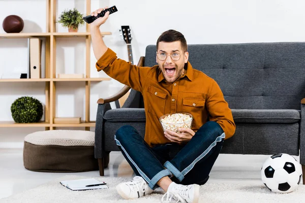 Aufgeregter Mann hält Schüssel mit Popcorn und schreit zu Hause — Stockfoto