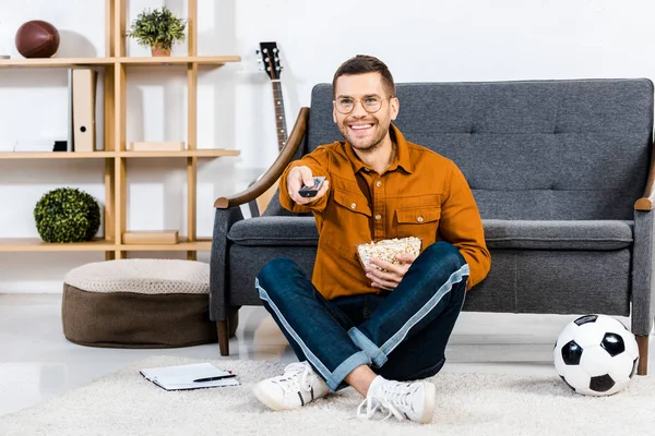 Smiling man holding bowl with popcorn and remote control in hands — Stock Photo