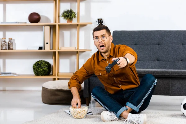 Шокований чоловік дивиться телевізор і сидить біля миски з попкорном — стокове фото