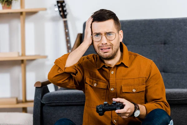 Hombre molesto en gafas sosteniendo gamepad después de jugar videojuego - foto de stock