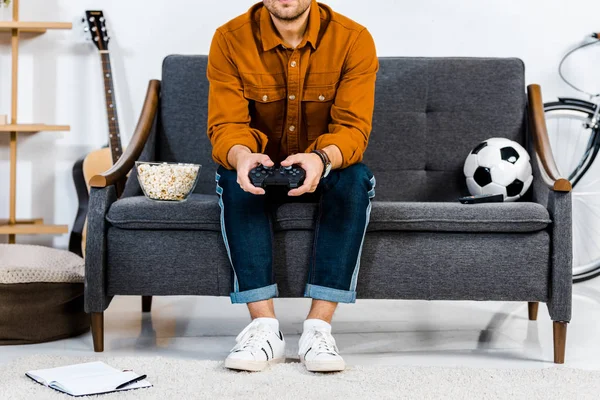 Cropped view of man sitting on sofa and playing video game — Stock Photo