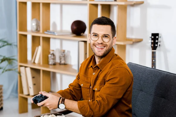 Веселий чоловік в окулярах тримає геймпад у вітальні — стокове фото