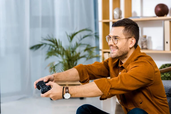 Homme heureux dans des lunettes jouer à un jeu vidéo à la maison — Photo de stock