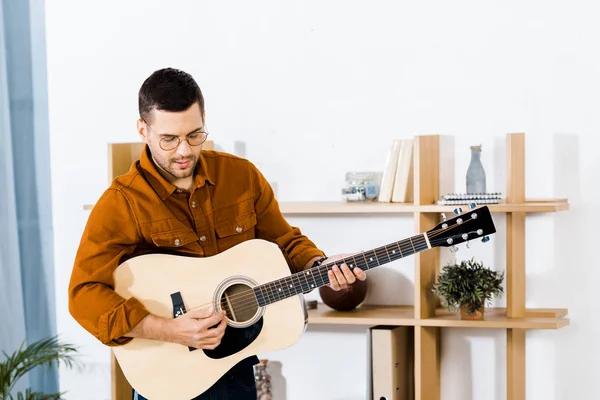 Красивый музыкант играет на акустической гитаре дома — стоковое фото