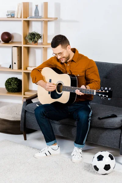 Guapo músico en gafas tocando guitarra acústica en sala de estar - foto de stock