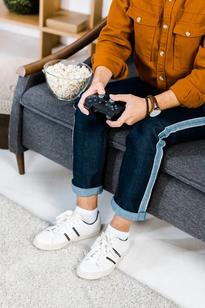 Обрезанный вид человека, играющего в видеоигру на диване — стоковое фото
