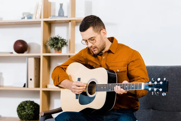 Bell'uomo in occhiali che suona la chitarra acustica in salotto — Foto stock