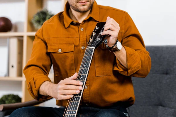 Обрезанный вид человека, настраивающего акустическую гитару дома — стоковое фото