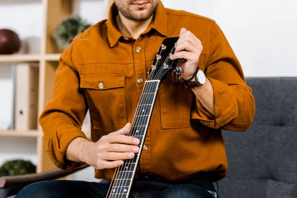 Visão cortada do homem afinando guitarra acústica em casa — Fotografia de Stock