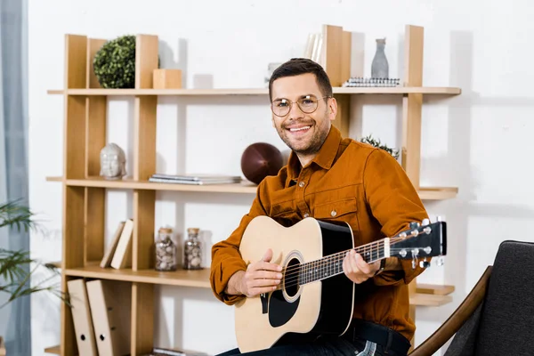 Homem feliz em óculos tocando guitarra acústica em casa — Fotografia de Stock