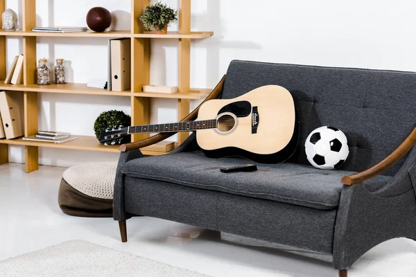 Moderna sala de estar con guitarra acústica, bola y control remoto en el sofá - foto de stock