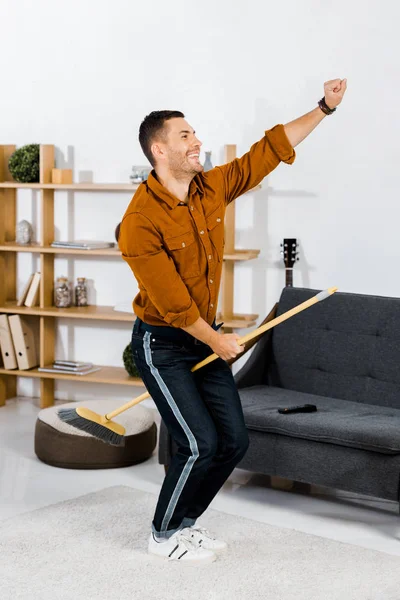 Hombre guapo divirtiéndose mientras limpia en la sala de estar moderna - foto de stock