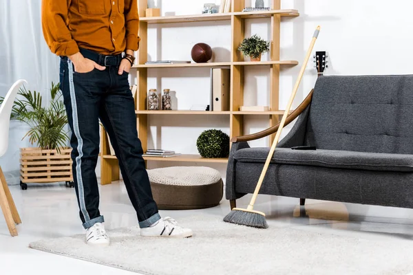 Cropped view of man standing near broom in modern living room — Stock Photo