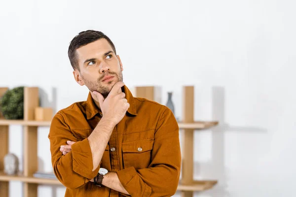 Hombre guapo de pie en la sala de estar moderna haciendo gesto de pensamiento - foto de stock