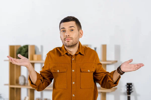 Handsome man standing in modern living room and doing confuse gesture — Stock Photo