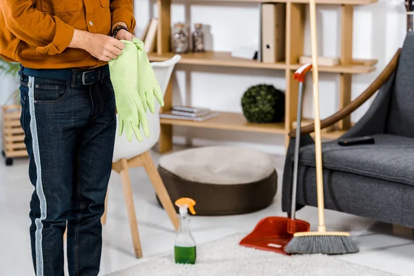 Ausgeschnittene Ansicht eines Mannes, der im Wohnzimmer steht und Gummihandschuhe aufsetzt — Stockfoto