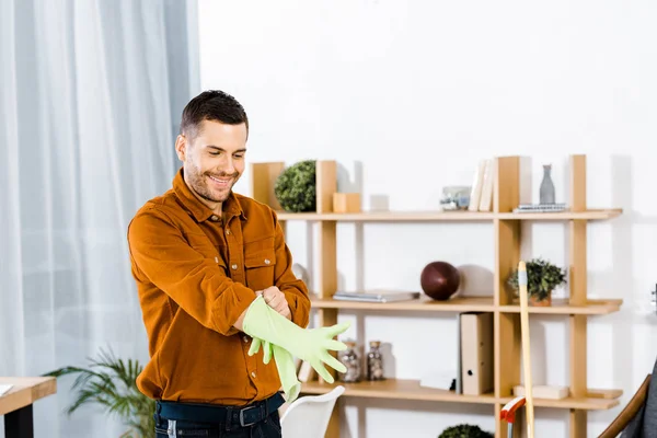 Homem bonito de pé na moderna sala de estar e colocar luvas de borracha — Fotografia de Stock