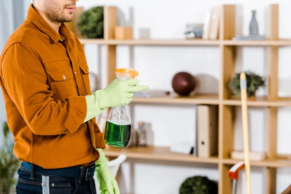 Cropped view of man standing in modern living room and holding bottle — Stock Photo