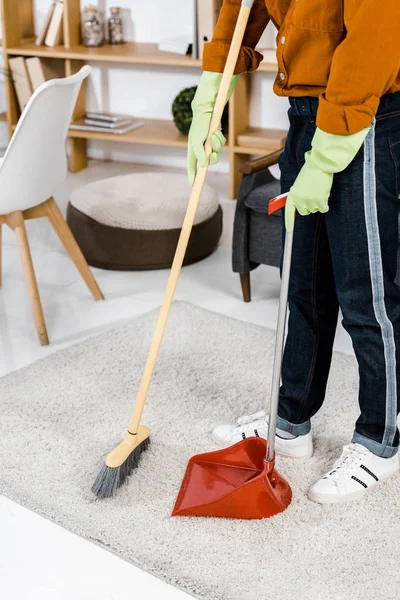 Abgeschnittene Ansicht eines Mannes, der im modernen Wohnzimmer steht und den Fußboden fegt — Stockfoto