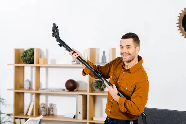 Hombre guapo en la sala de estar moderna levantándose aspiradora y sonriendo a la cámara - foto de stock