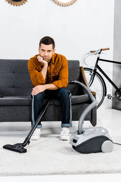 Hombre molesto en la sala de estar moderna sentado en el sofá y mirando a la cámara - foto de stock