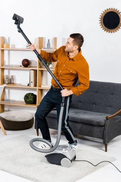 Hombre guapo en la sala de estar moderna sonriendo y levantándose hoover - foto de stock