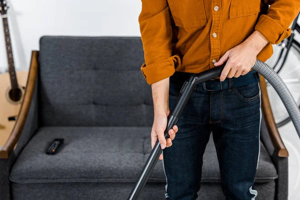 Vista ritagliata dell'uomo nel moderno soggiorno pulizia pavimento con aspirapolvere — Foto stock