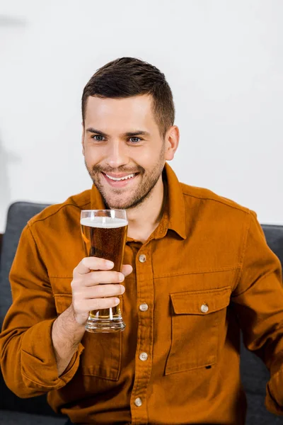 Schöner Mann im modernen Wohnzimmer sitzt auf dem Sofa und hält ein Glas Bier in der Hand — Stockfoto