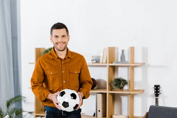 Bell'uomo in piedi in salotto moderno e tenendo palla da calcio — Foto stock
