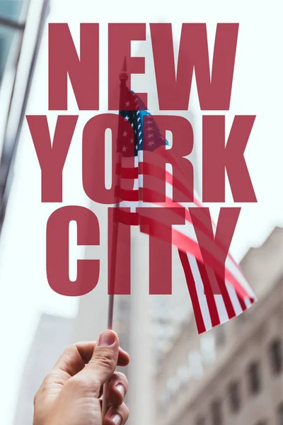Recortado disparo de hombre sosteniendo bandera americana en la mano con borrosa calle de la ciudad de Nueva York en el fondo con letras de la 