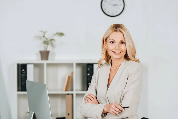 Belle femme d'affaires mature debout avec les bras croisés et souriant à la caméra dans le bureau — Photo de stock